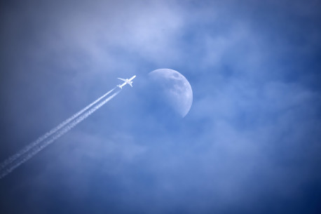 Flugzeug mit Kondensstreifen streift den Mond am Himmel.